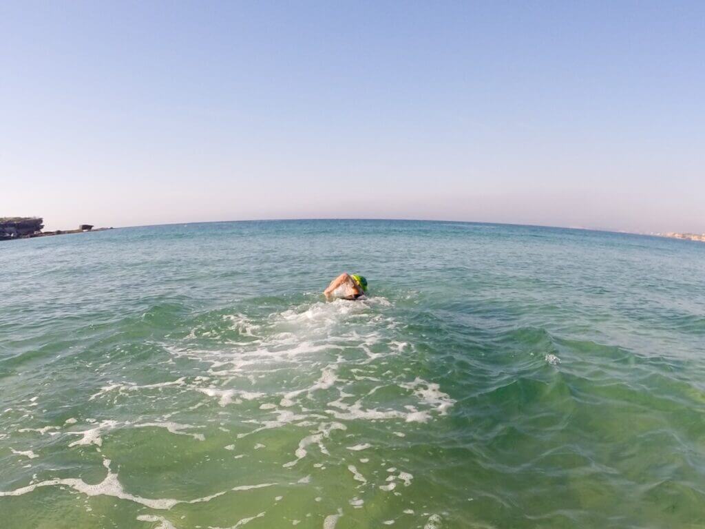 A solo swimmer swimming away from the beach, out to sea.