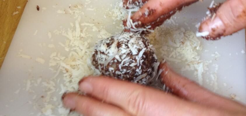 Protein ball is being dipped in coconut and rolled on a plate.