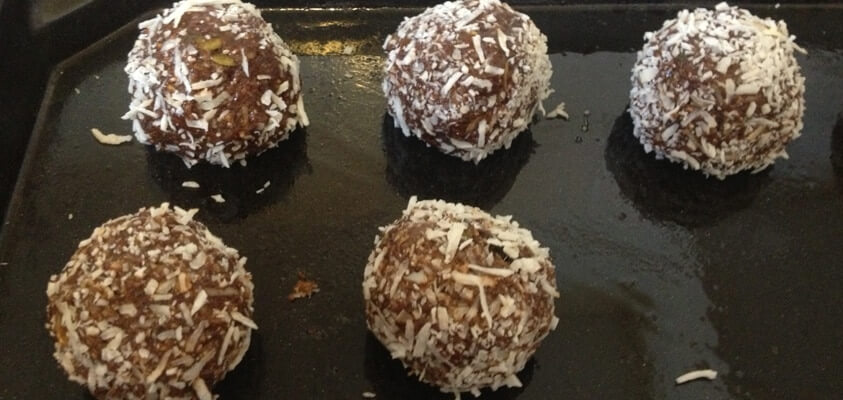 Five protein balls are lined up on a baking tray ready for the oven.