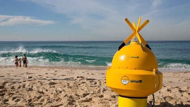 A metal yellow buoy sits on the beach ready to be put into the water.